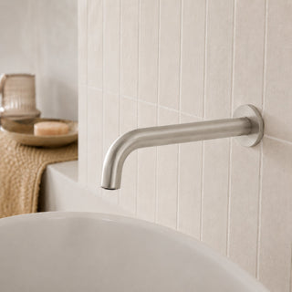 nickel bathroom wall spout tap in a modern bathroom with beige tiles and a free standing bath